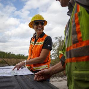 Terri Hall points to a map laid on the tailgate of a truck, smiling at another crew member