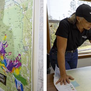 Terri in an office, pointing to a map on a wall, and looking at at map on a table with another person.