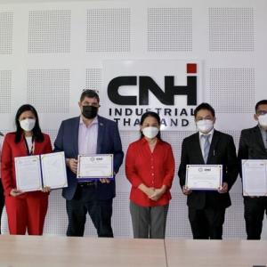 Group of people, all wearing protective masks, stand in front of CNHI sign in a conference room. Some hold documents