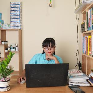 Thao sitting at a desk with a laptop. Shelves of books and products around her.