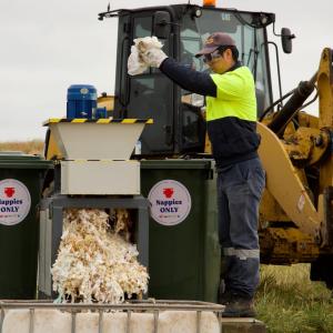 A person loading diapers into a bin with stickers 'nappies only.'