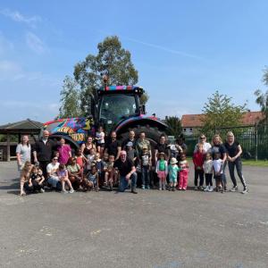 A large group of children and adults stood together in front of a colourful tractor