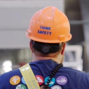 A person walking away, "Think Safety" on the back of their hard hat.