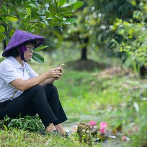 Thoa Nguyen sitting in an orchard using a cell phone.