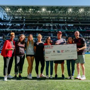 People stood on a soccer pitch holding a cheque 