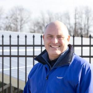 A person standing in front of a fenced-off solar panel field