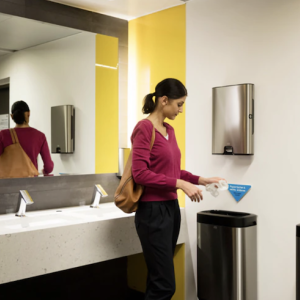 A woman standing in a bathroom using a paper towel.
