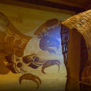 Bird of prey depicted in inlaid wood beside a basket woven out of cedar bark.