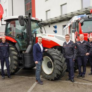 Six people stand arounf a large tractor and fire truck outside.