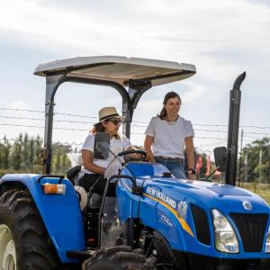 One person sat in a blue tractor with another person stood at the side