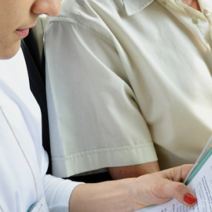 One person writing on a piece of paper with another person stood next to them looking over