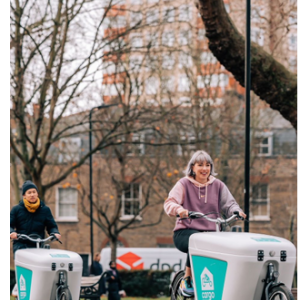 Two people riding bikes outside with carriers in front.