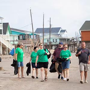A group of people, some in matching shirts, walking on a beach with trash bags.