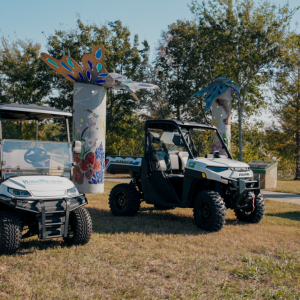 Two UTVs are parked in a grassy sunny area.