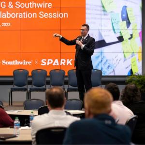 A speaker in front of a room of seated people. A digital screen behind with "UWG & Southwire Collaboration Session" 