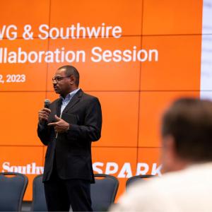 A speaker in front of a room of seated people. A digital screen behind with "UWG & Southwire Collaboration Session" 