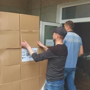 two people moving stacks of boxes inside open doors of a building