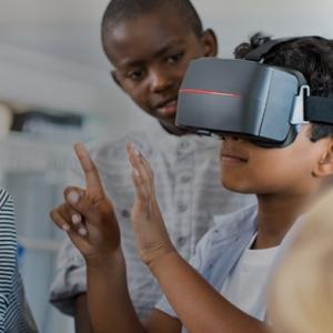 Children watch as another uses a VR headset.