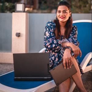 Vishakha Fulsunge in a dress sitting next to a Lenovo laptop and holding a tablet