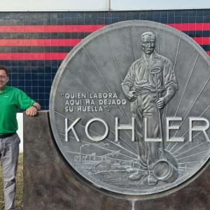 Vitor Wojastyk standing next to a large sign at the entrance of the Kohler plant