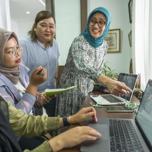 Four women talking as one uses a laptop at a desk.