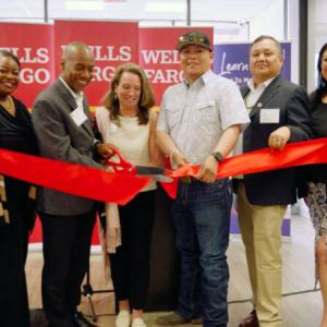 Group of people standing inside a brank branch cutting a red ribbon