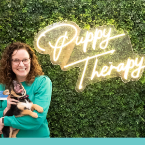 Woman holding dog with the words, "Puppy Therapy" behind them