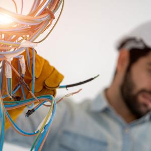 Electrical worker shown wearing a helmet and working on wiring.