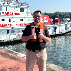 Wesley Rhoden wearing a life vest standing on a pier, a Marathon boat behind them.