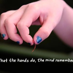 "what the hands do, the mind remembers." with a hand holding a tiny worm