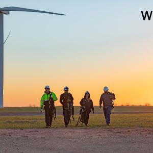 four workers in safety gear walking in front of wind turbines at dawn