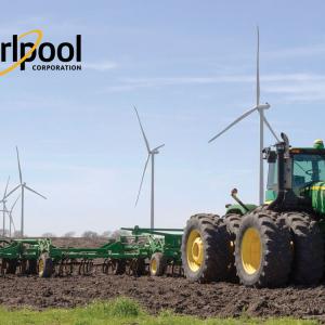 A large green tractor tills a field, wind turbines behind it in a row. Whirlpool logo in the upper left.
