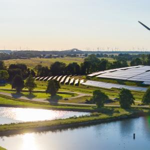 Windmill and solar panel farm shown with a water source in the foreground.