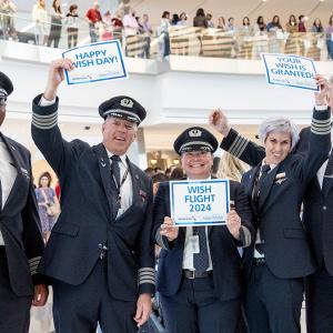 Five cheering pilots holding signs in an airport "Wishes come true" "Happy Wish Day" and "Wish flight 2024."