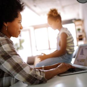 woman working on a laptop with a child in the background