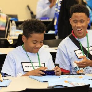 A group of kids in matching shirts talking and smiling, seated at a long table.