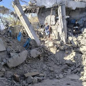People stand on a pile of rubble that used to be the Huqah health facility 