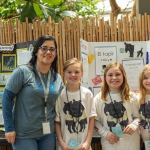 An adult and three students standing in front of display boards.