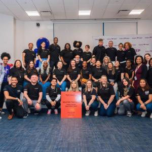 A group of me and woman wearing black shirts stand and kneel looking directly at the camera