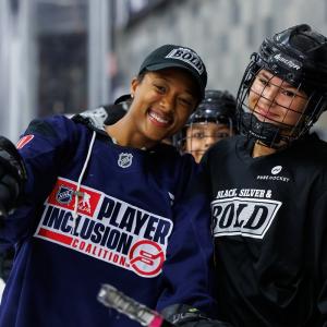 Blake Bolden in a Player Inclusion Coalition jersey poses with a participant in Black, Silver & Bold gear during a hockey clinic.