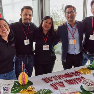 A group of five people with arms around each other. A table with pens and decorations in front of them.