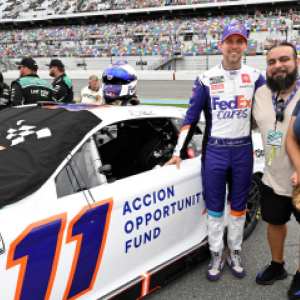 Three people standing next to a race car, number 11,  on a track.