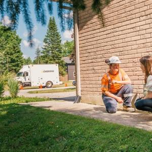 utility worker and homeowner crouched near a home and talking