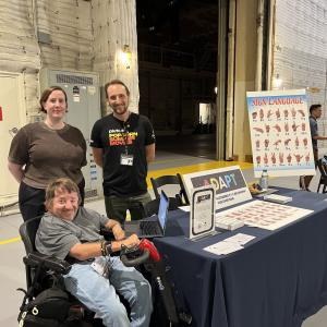 Three people by a table with ADAPT literature and an asl board.