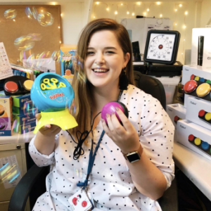 A person holding up a bubble machine and colorful button, colorful products on a desk behind them.