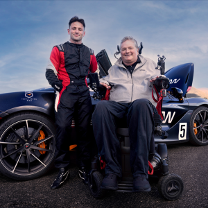 A person leaning against a car and a person in a wheelchair next to them 