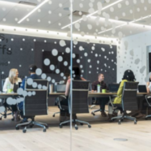 Through clear glass walls, people seated at a conference table.