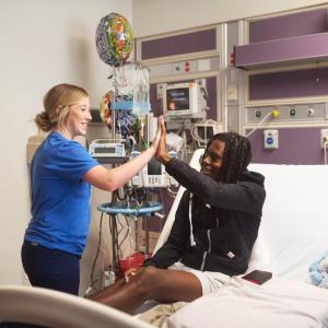Patient sitting in a bed giving a high five to a nurse.