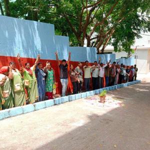 A line of people raising their hands and smiling, against a red and white wall