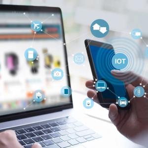 A hand holding a device and another using a laptop.